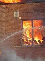 Brick school building window with interior on fire and smoke being extinguished