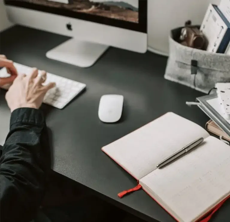 Person working at a desktop computer with planner and documents on black desk representing nonprofit tech assistance