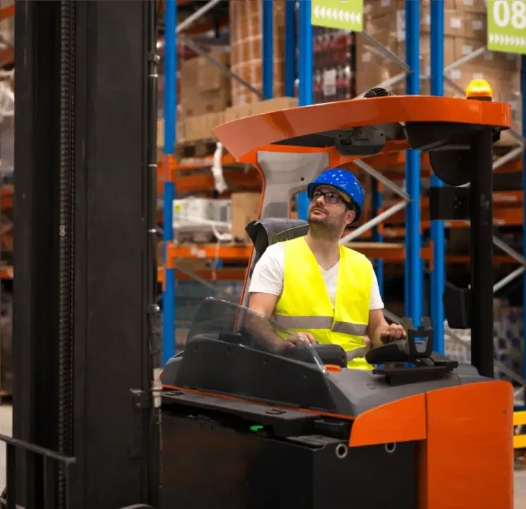 Warehouse worker operating a forklift looking upward for inventory while wearing a safety vest and hard hat